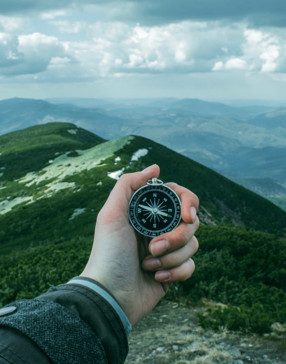 Arm holding compass out overlooking mountainous terrain